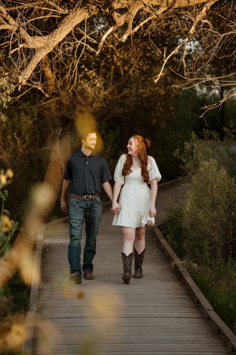 Abby and Collin walking hand in hand under the oak trees