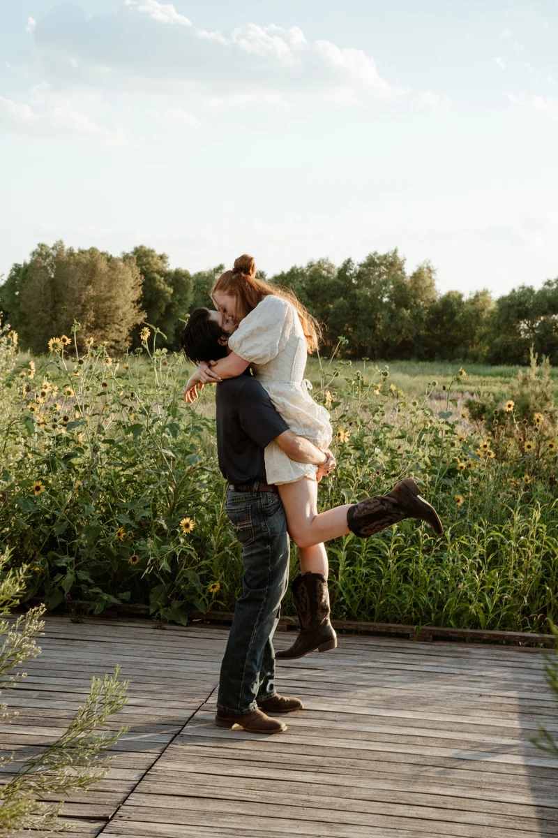 Collin lifting Abby off her feet beside the sunflower field